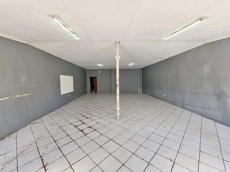 An empty, open-plan commercial space featuring tiled flooring, a central structural column, and fluorescent lighting, suitable for retail or office use.