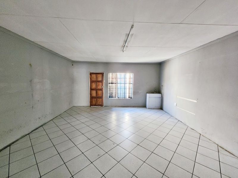 An empty, open-plan commercial space featuring tiled flooring, a small basin, and security bars on the window, ready for renovation or fit-out.