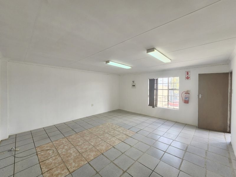 A vacant commercial office space featuring tiled flooring, fluorescent lighting, and essential safety equipment including a fire extinguisher.