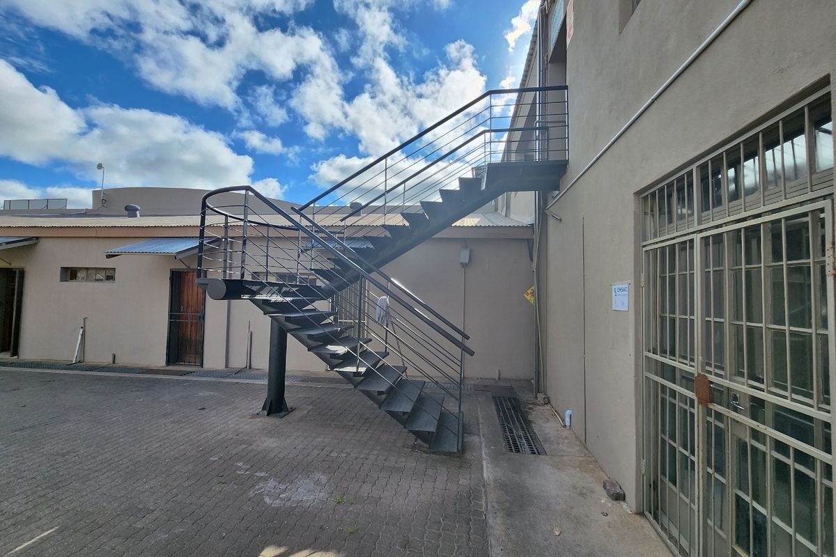 Rear exterior view of the commercial property featuring a paved courtyard and an external metal staircase providing access to the upper level.