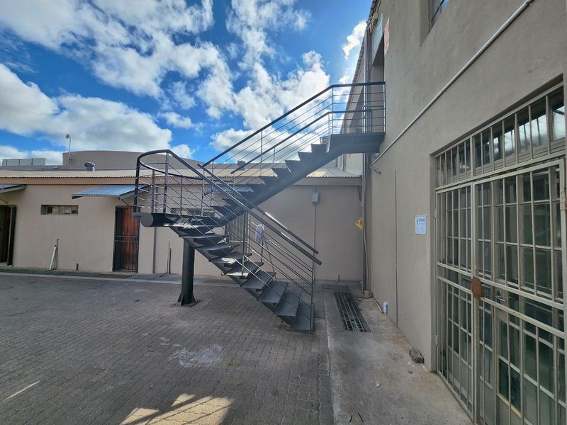 Rear exterior view of the commercial property featuring a paved courtyard and an external metal staircase providing access to the upper level.