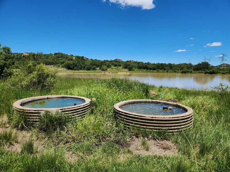 Two circular concrete water troughs situated in a grassy field overlooking a natural farm dam.