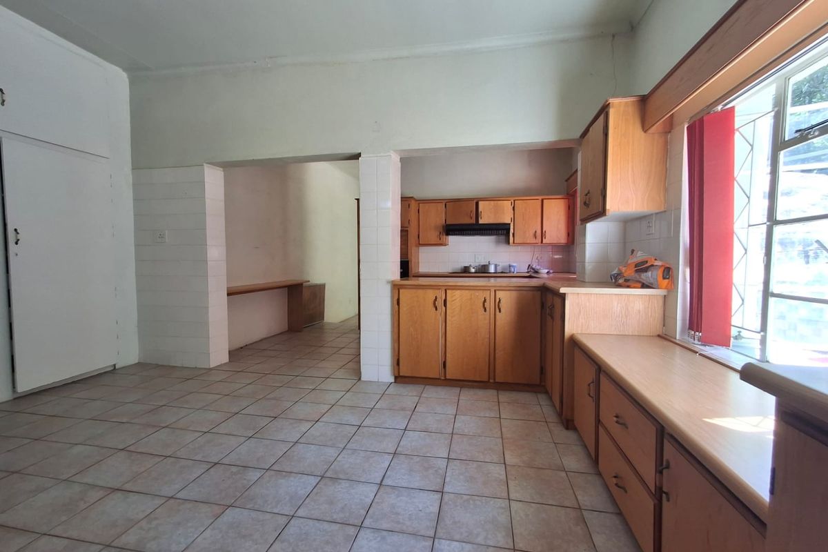 A spacious, dated kitchen featuring wooden cabinetry, tiled flooring, and an open-plan layout with an adjacent utility area.