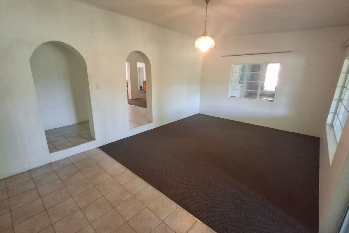 An empty living room featuring arched doorways, a mix of tiled and carpeted flooring, and a central pendant light fixture.