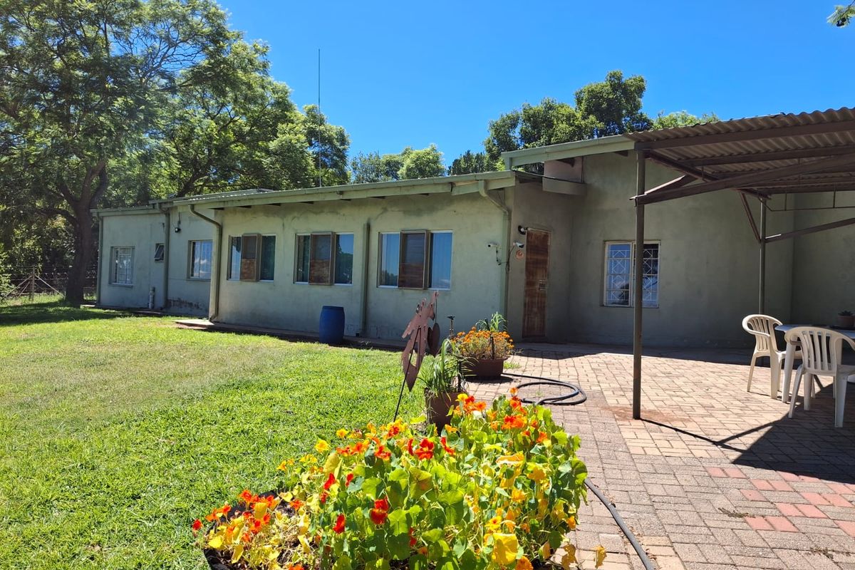 Rear view of the farm dwelling featuring a paved patio area, established garden, and corrugated metal roofing.