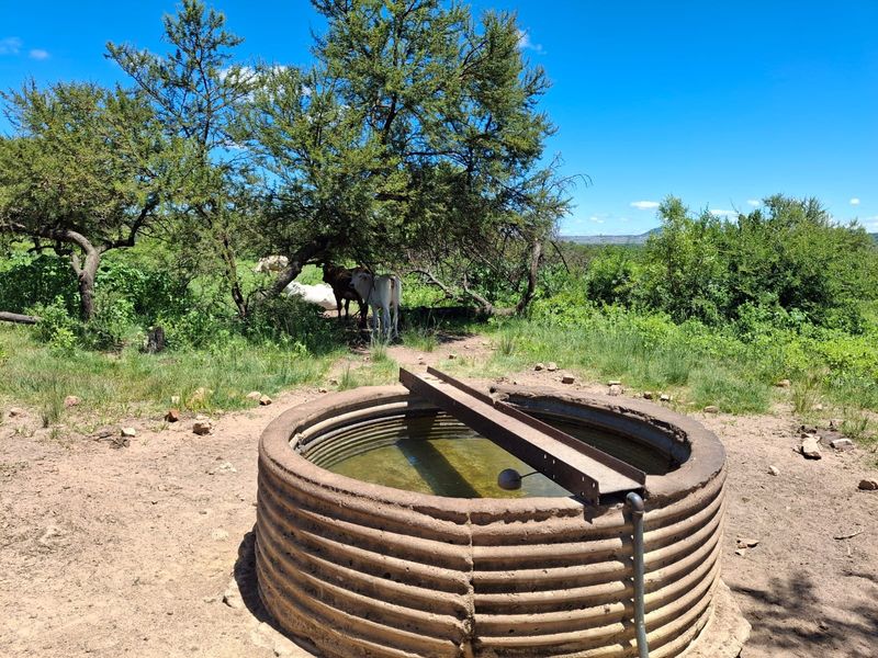 A rustic corrugated steel water reservoir located in a rural farm setting, featuring a float valve and metal support structure.