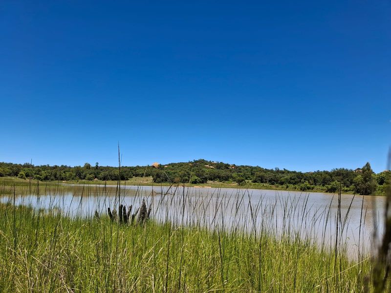 A scenic view of a natural dam surrounded by lush green vegetation and rolling hills under a clear blue sky.