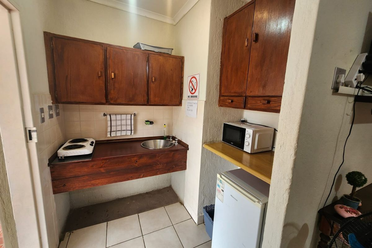 A compact kitchenette featuring built-in wooden cabinetry, a stainless steel sink, tiled flooring, and a tiled backsplash, suitable for a small holding unit.