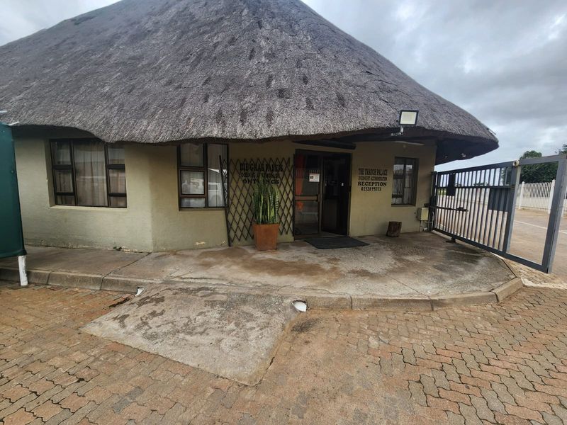 Front entrance of a thatched building featuring a paved driveway, security gate, and concrete access ramp.