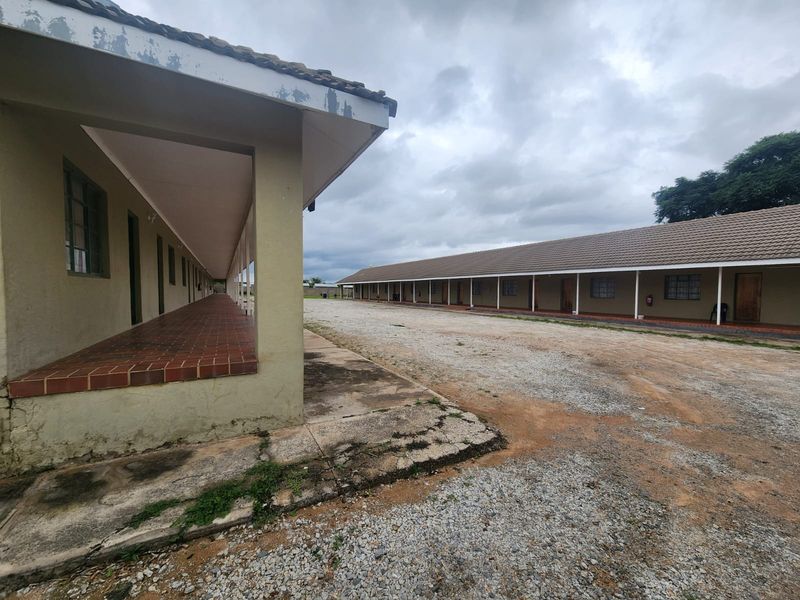 Exterior view of a small holding featuring long, covered walkways with tiled verandas and a large gravel courtyard area between the buildings.