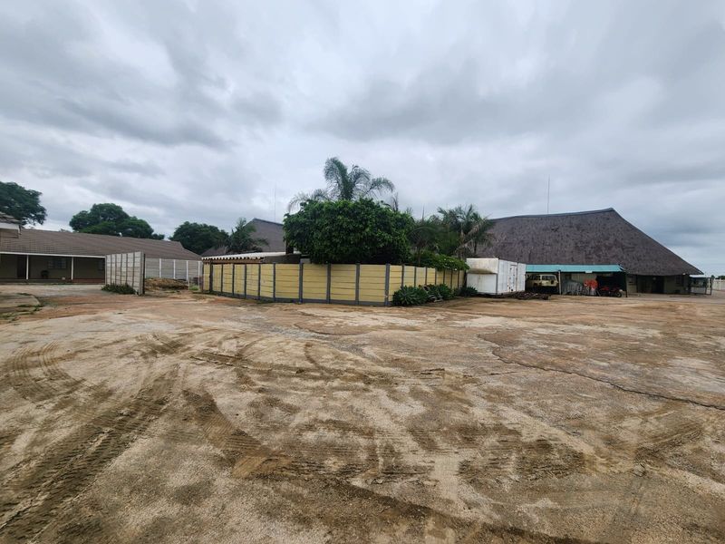 Expansive rear yard area featuring a large concrete surface, precast boundary walls, and access to multiple structures with traditional thatched roofing.