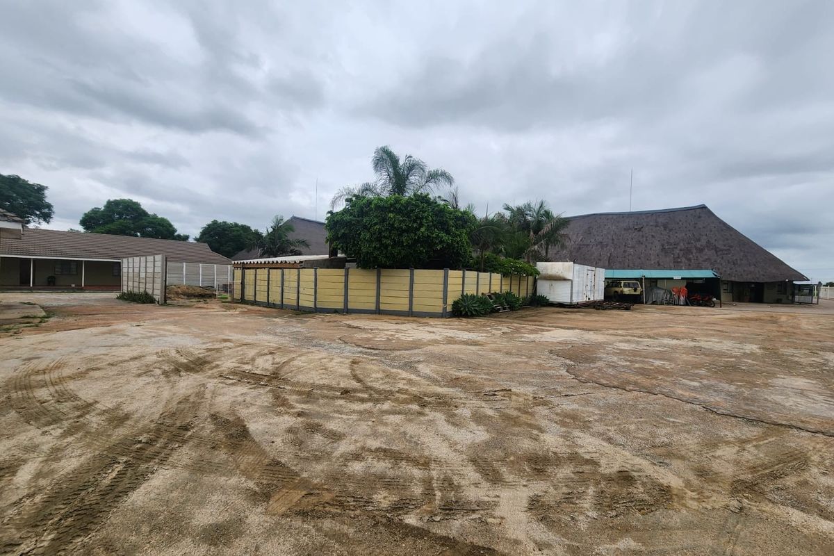Expansive rear yard area featuring a large concrete surface, precast boundary walls, and access to multiple structures with traditional thatched roofing.