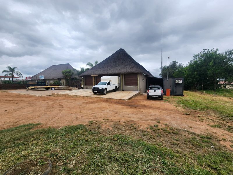 Front view of a small holding property featuring a thatched roof building with roller shutter doors and a concrete driveway area.