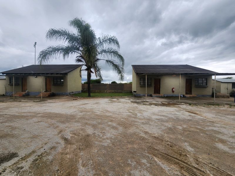 Front view of two detached residential units on a small holding, featuring tiled roofs, covered patios, and an unpaved driveway area.