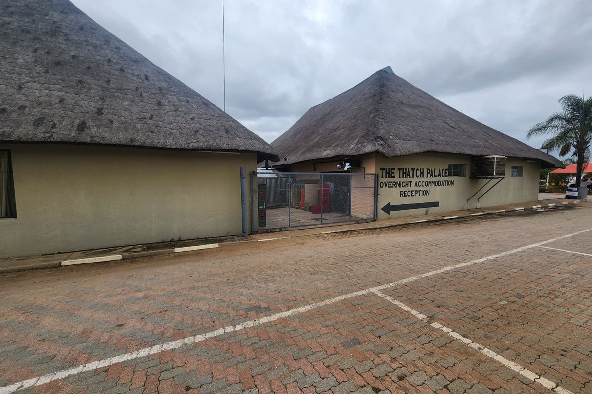 Exterior view of The Thatch Palace reception area featuring traditional thatched roofing and paved parking area.