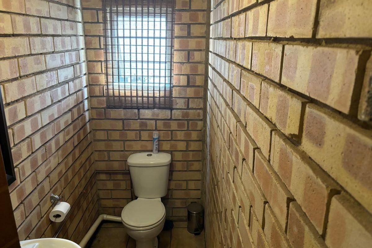A compact industrial-style bathroom featuring exposed brick walls, a standard ceramic toilet, and a small basin.