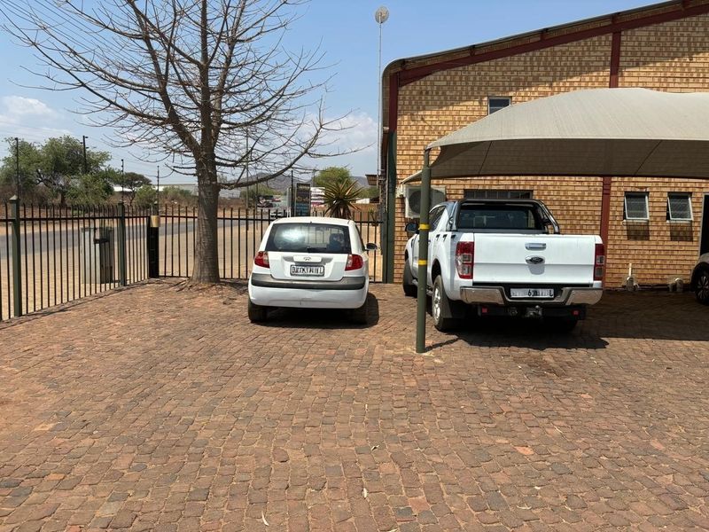 Industrial property exterior featuring a brick facade, paved parking area, and a shade cloth carport structure.
