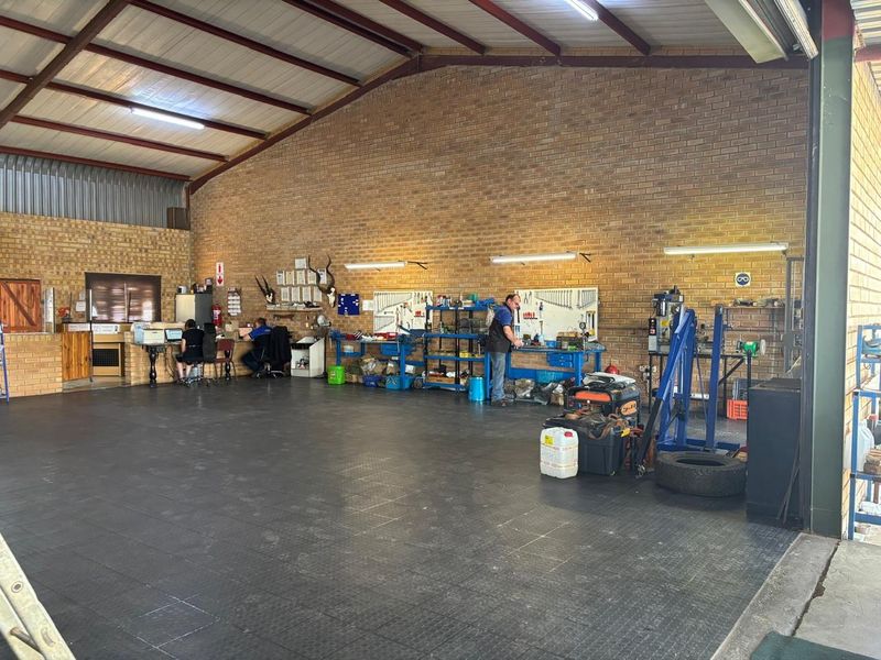 Spacious industrial workshop featuring exposed brick walls, steel roof trusses, durable rubberized flooring, and integrated workbench areas suitable for professional mechanical or industrial operations.