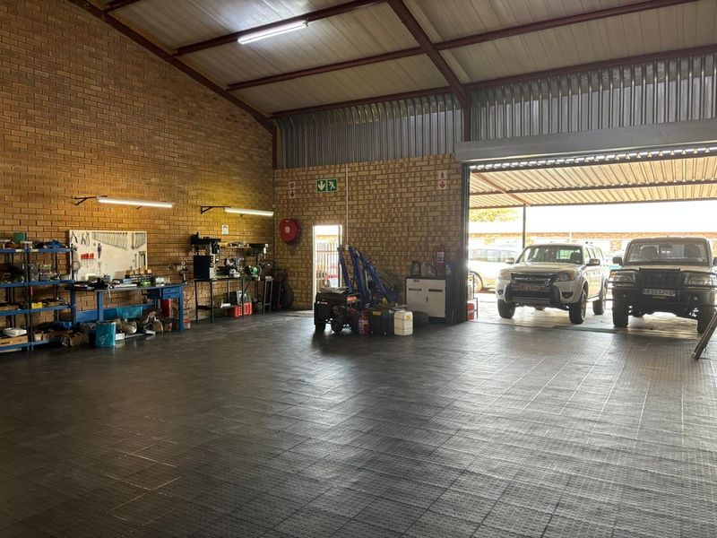 Spacious industrial garage featuring exposed brick walls, steel roof trusses, and durable industrial flooring, suitable for workshop or storage use.