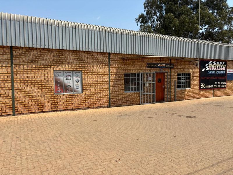 Front elevation of an industrial workshop featuring face brick construction, a curved metal roof, and a paved forecourt with signage.