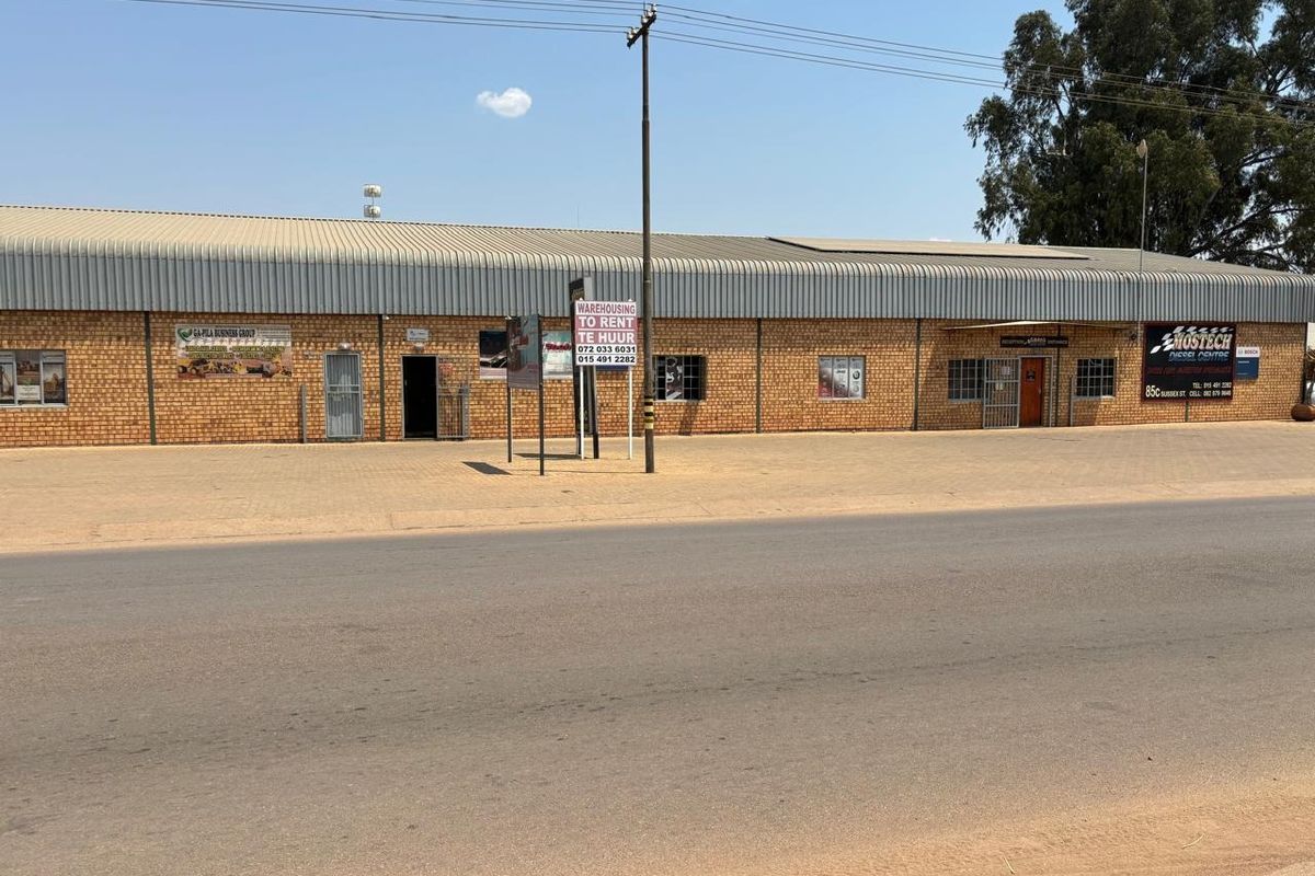 Front elevation of an industrial warehouse property featuring face brick construction, corrugated metal roofing, and multiple access points with security gates.