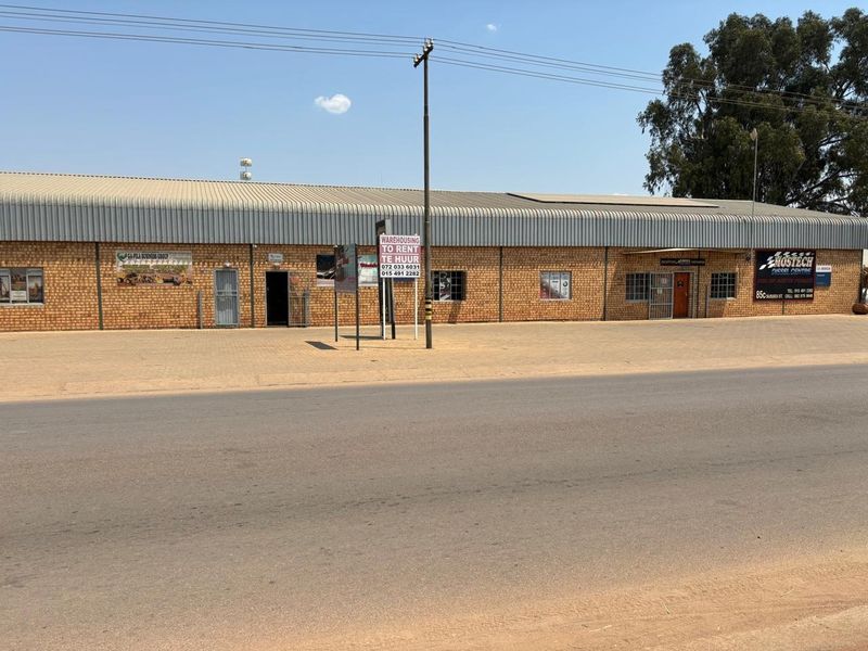 Front elevation of an industrial warehouse property featuring face brick construction, corrugated metal roofing, and multiple access points with security gates.