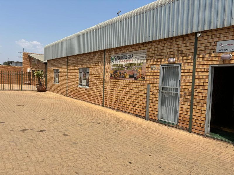 Industrial property exterior featuring a face brick facade, corrugated metal roofing, and a paved driveway with secure access points.