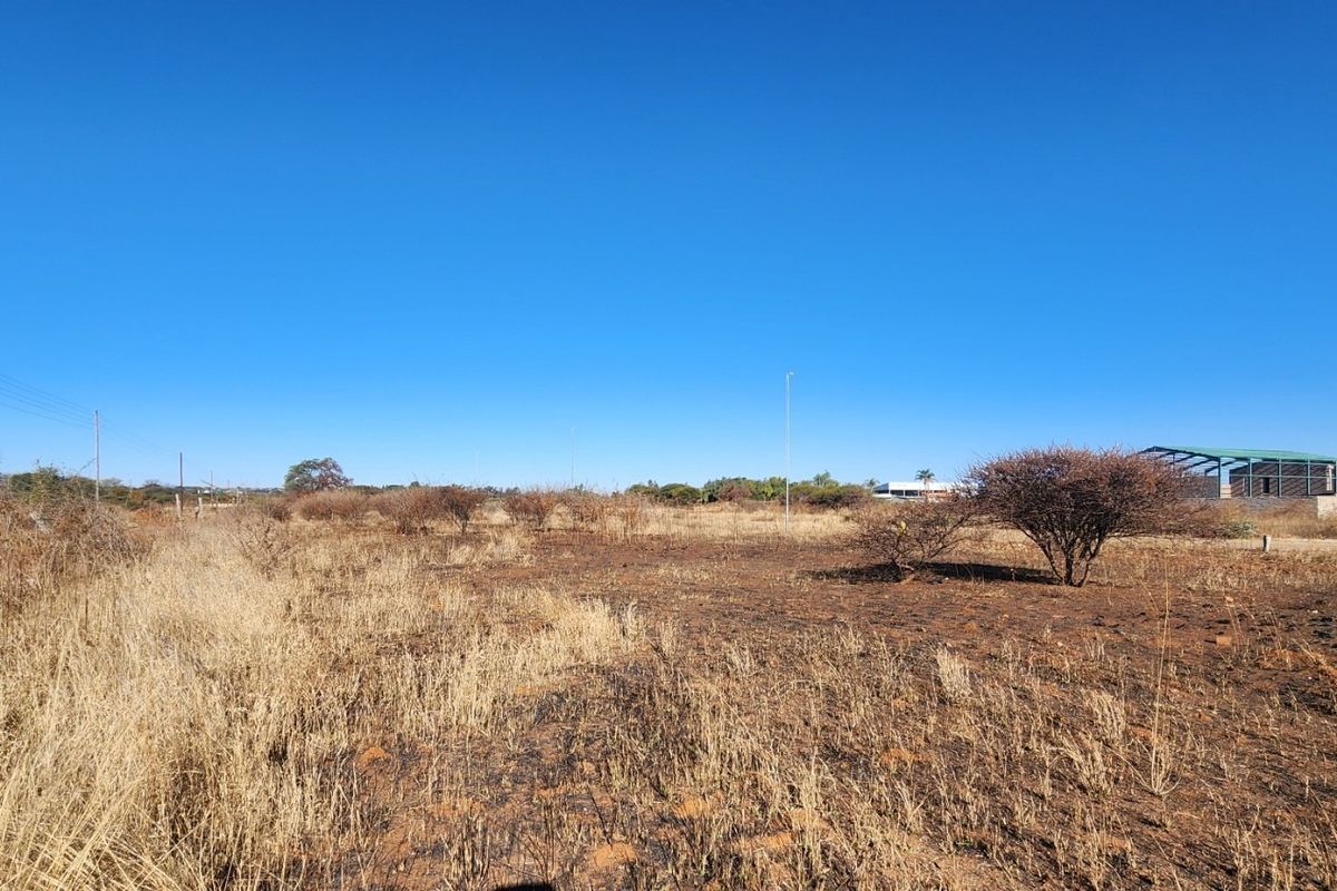A wide-angle view of a vacant commercial land plot featuring dry vegetation, open space, and existing utility infrastructure.