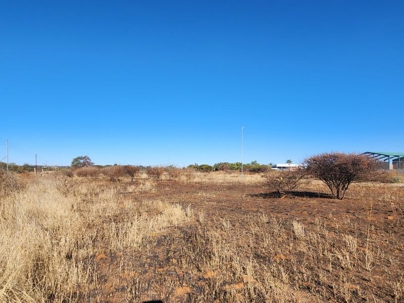 A wide-angle view of a vacant commercial land plot featuring dry vegetation, open space, and existing utility infrastructure.