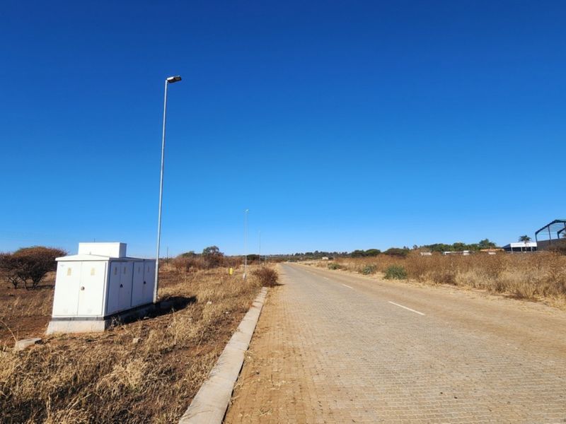 A view of a paved commercial access road featuring installed street lighting and an electrical utility box on the roadside.