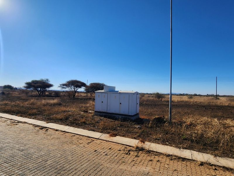 A view of a vacant commercial plot featuring a paved road, concrete curbing, and an installed electrical distribution box.