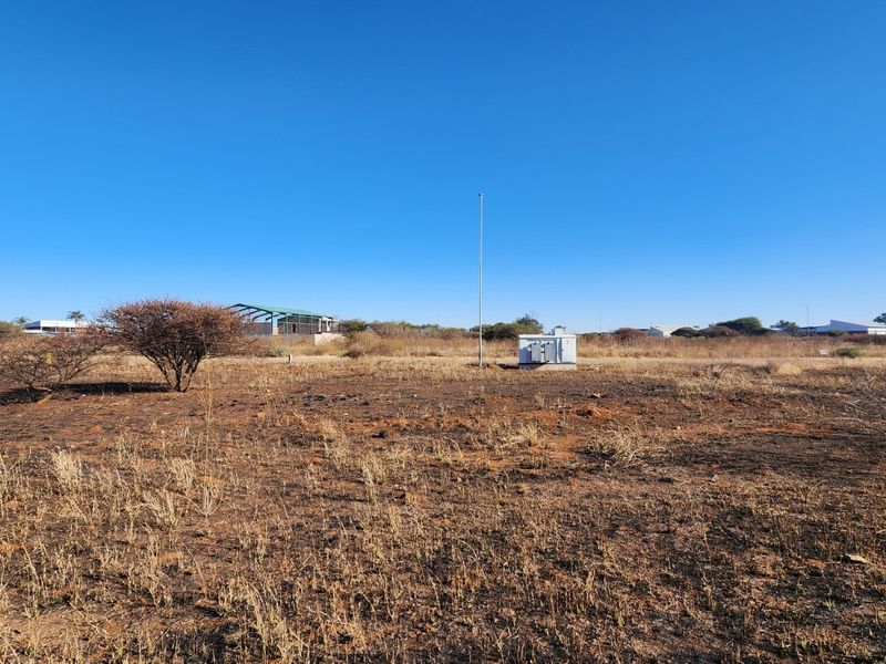 A view of a vacant commercial land plot featuring dry vegetation, a utility pole, and an electrical transformer box.