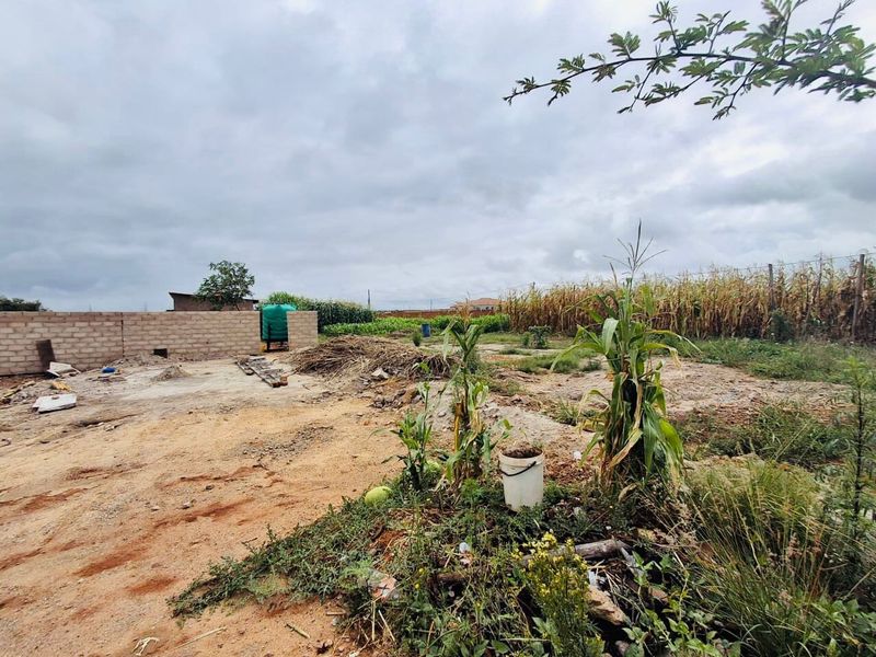 A view of a vacant commercial plot featuring a partial concrete block boundary wall and a water storage tank on site.