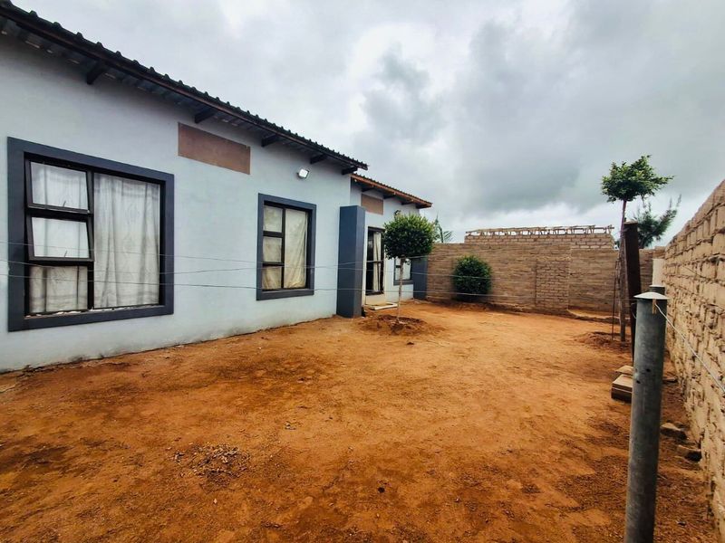 Rear view of the property featuring a large unlandscaped yard, brick boundary walls, and a single-story building with aluminium window frames.