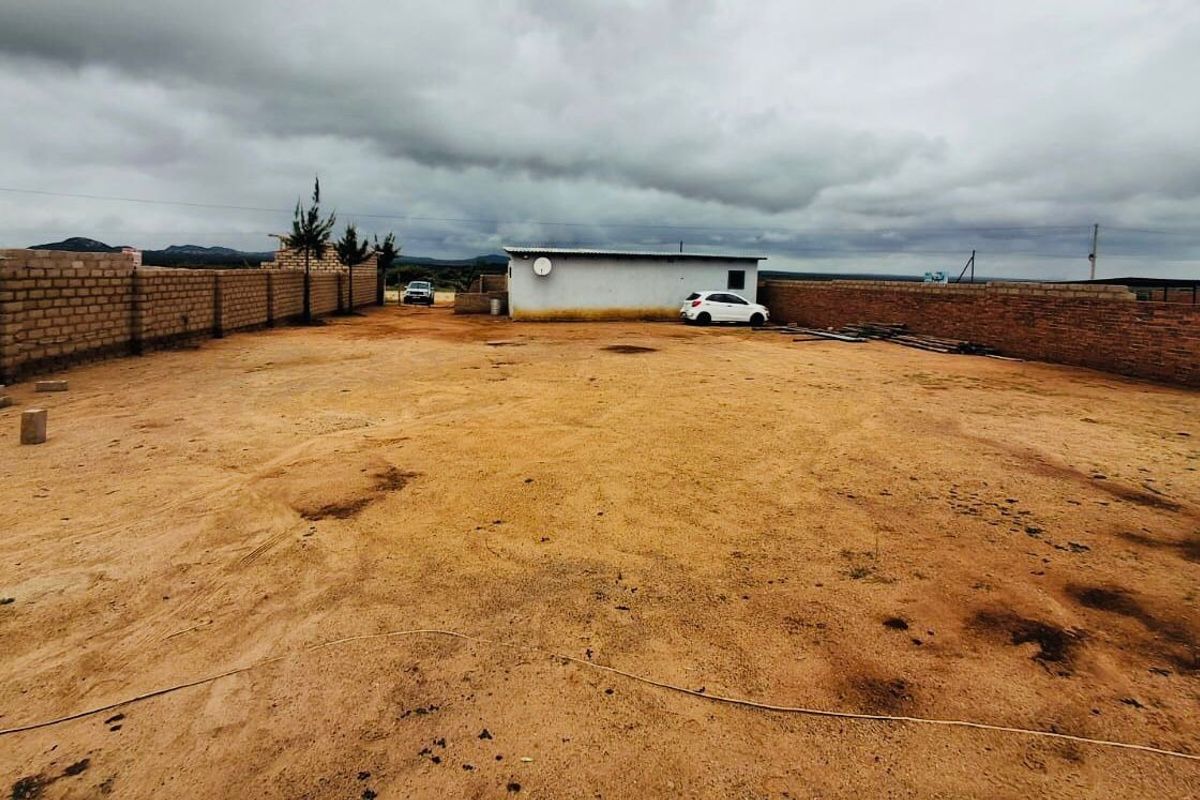 A large, open, unpaved commercial plot enclosed by perimeter brick walls, featuring a small outbuilding structure.