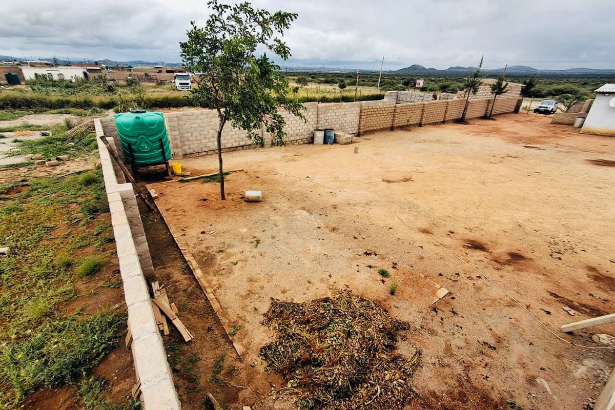 A view of the rear yard area featuring a perimeter wall and a water storage tank on a large, unpaved plot of land.