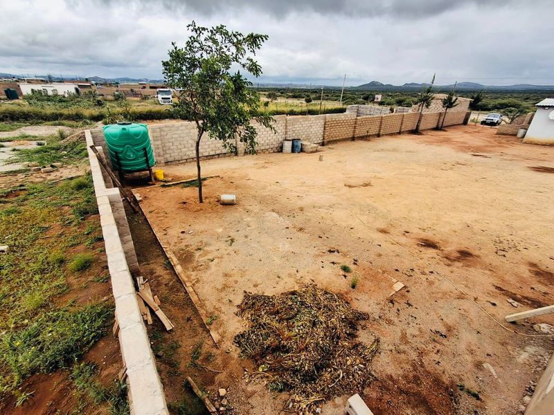 A view of the rear yard area featuring a perimeter wall and a water storage tank on a large, unpaved plot of land.