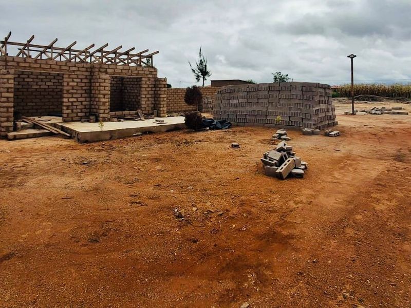 A vacant commercial land plot featuring an incomplete concrete block structure with timber roof framing and scattered building materials on site.
