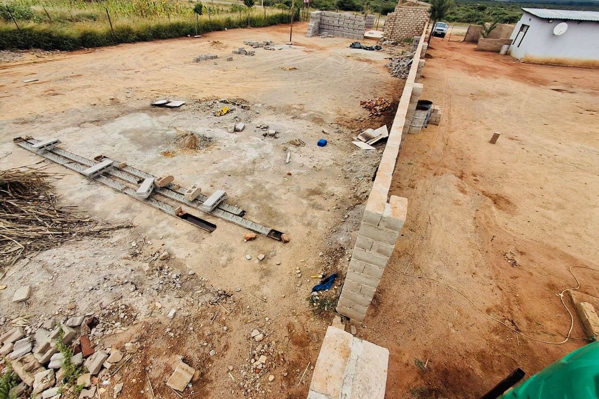 An elevated view of a vacant commercial plot featuring a perimeter wall and ongoing foundation construction work.