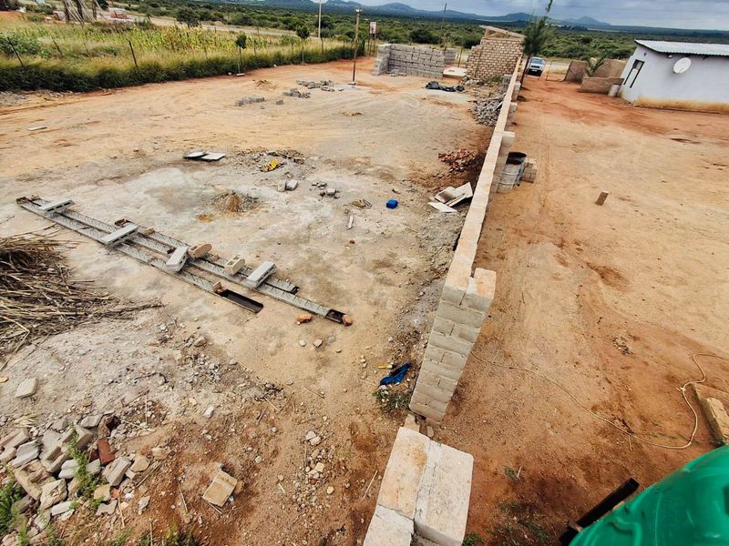 An elevated view of a vacant commercial plot featuring a perimeter wall and ongoing foundation construction work.