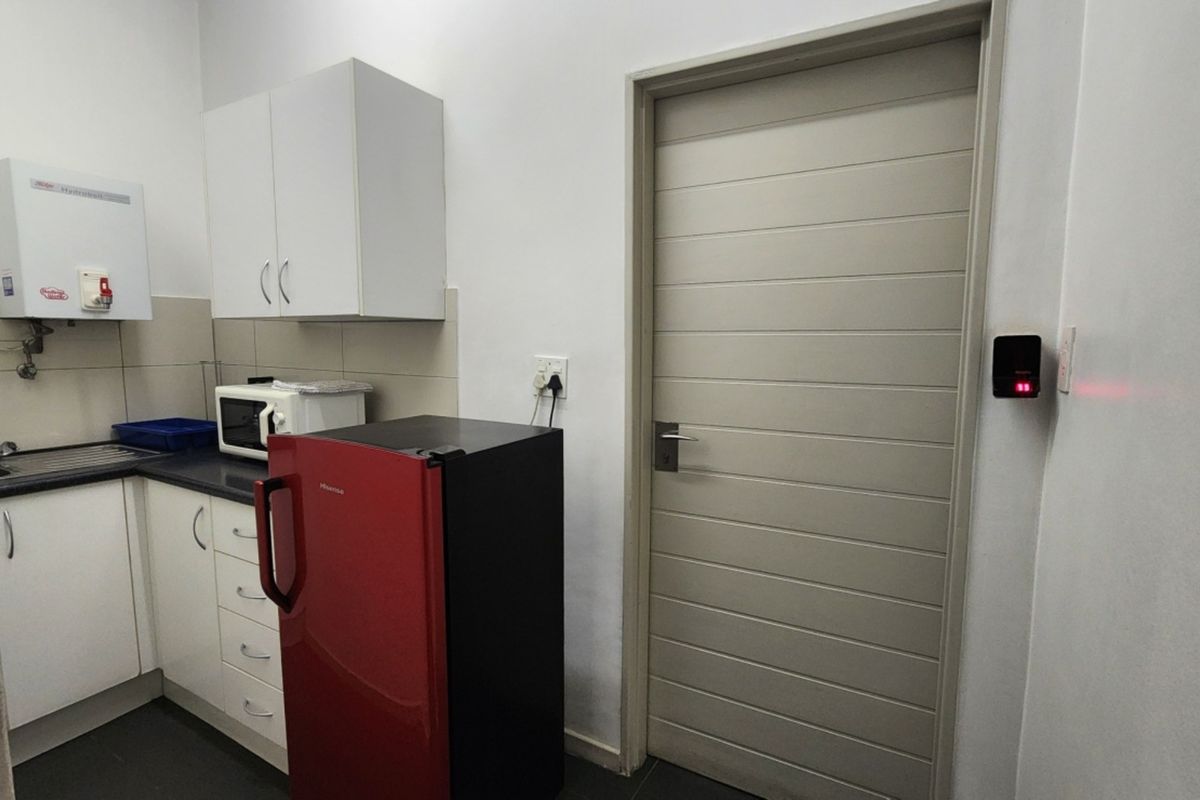 A compact kitchen area featuring white built-in cabinetry, a sink, a wall-mounted water heater, and a neutral-toned internal door.