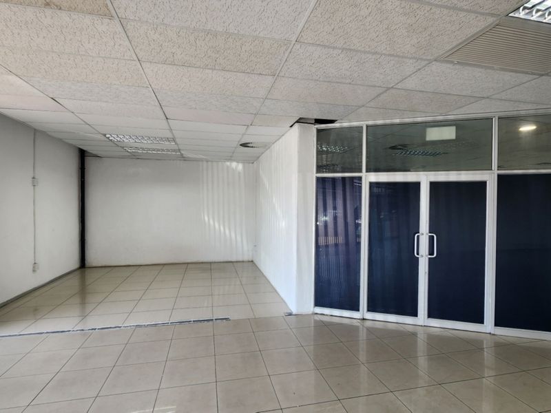 An empty open-plan retail space featuring ceramic tiled flooring, a suspended ceiling with recessed lighting, and a glass-partitioned entrance.