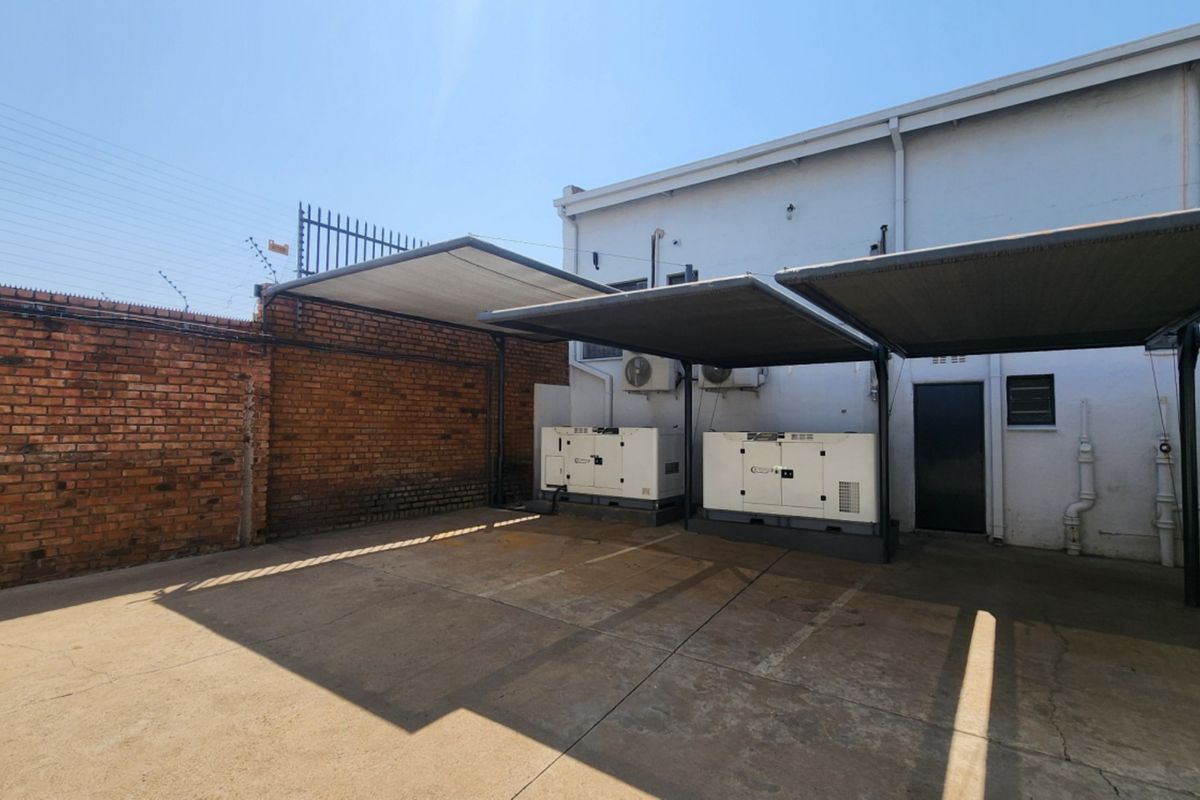 Rear exterior area featuring a paved parking space with shade cloth carports, industrial generators, and secure brick boundary walling.