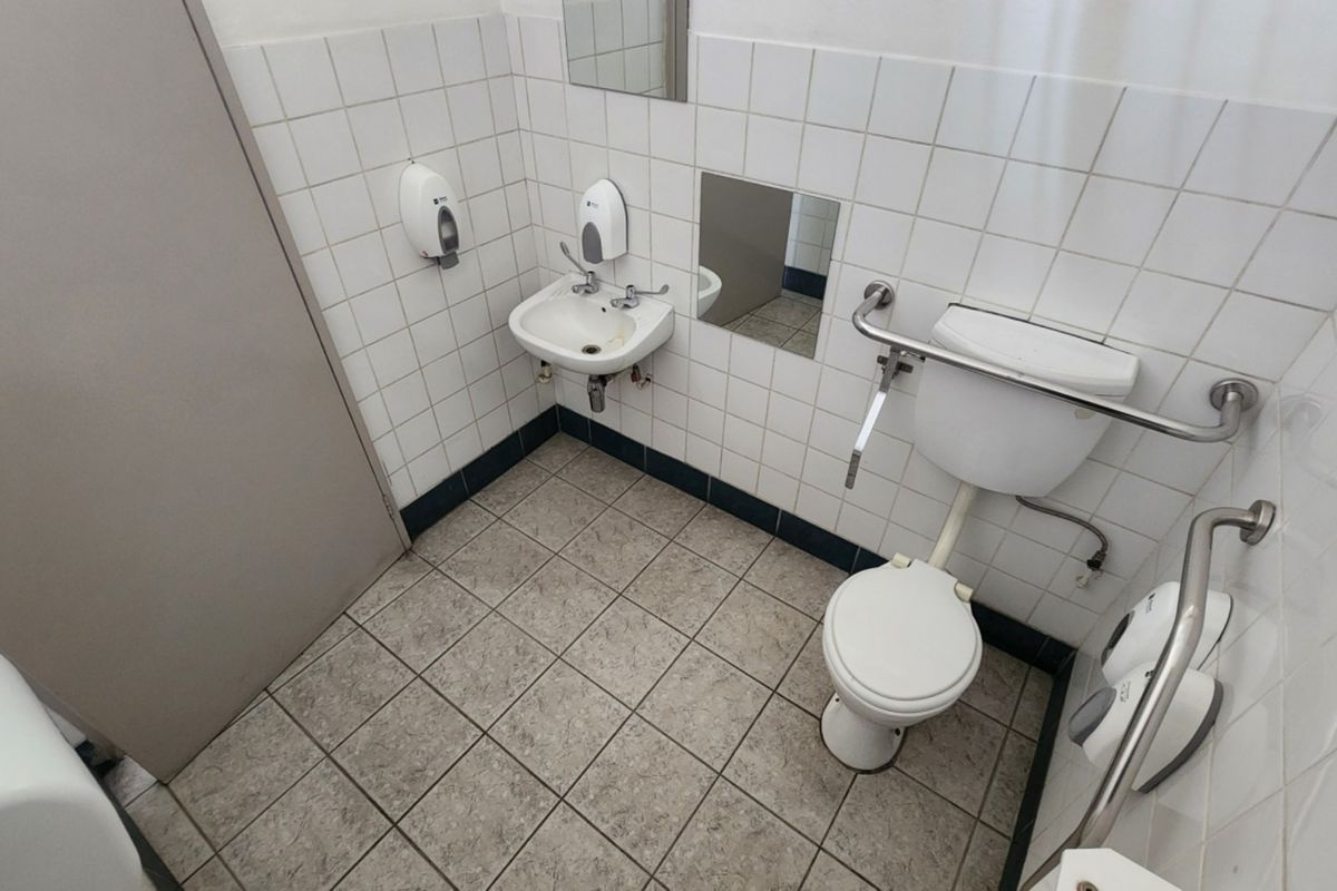 A functional, accessible bathroom featuring tiled walls and flooring, a wall-mounted basin, toilet, and safety grab rails.