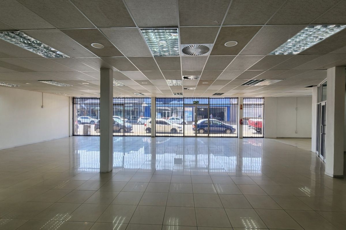 Spacious open-plan retail unit featuring polished ceramic tile flooring, a suspended ceiling with recessed lighting, and a secure glass storefront.