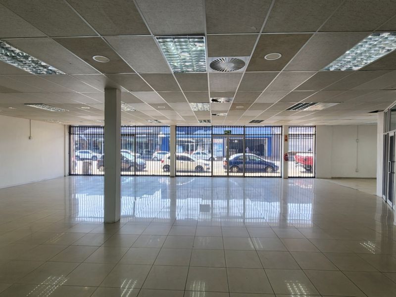 Spacious open-plan retail unit featuring polished ceramic tile flooring, a suspended ceiling with recessed lighting, and a secure glass storefront.