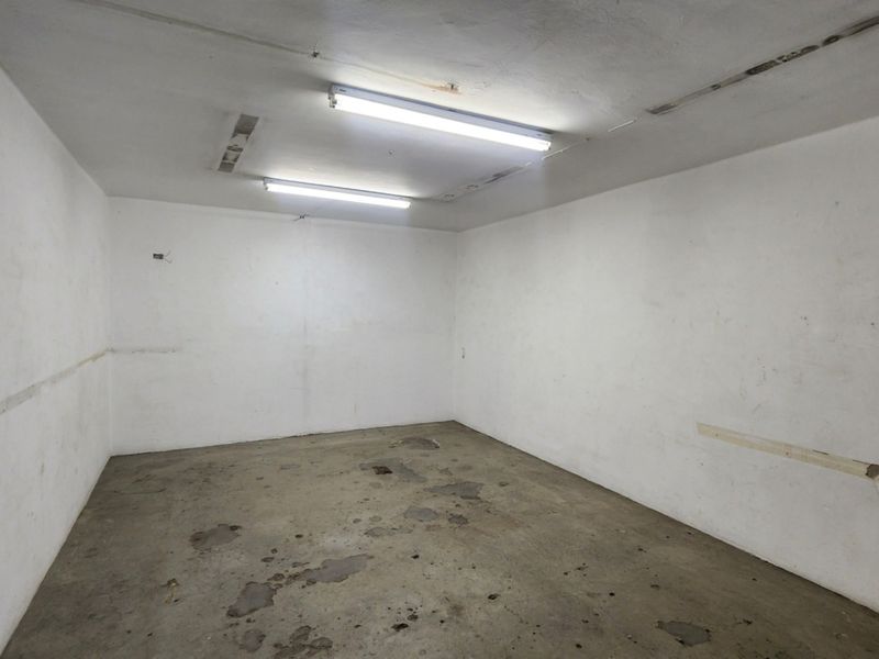 An empty, utilitarian storage or utility space featuring concrete flooring and fluorescent overhead lighting, requiring cosmetic refurbishment.