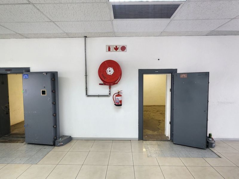 Utility area featuring two heavy-duty vault doors, a fire hose reel, and a fire extinguisher, with tiled flooring and a suspended ceiling.
