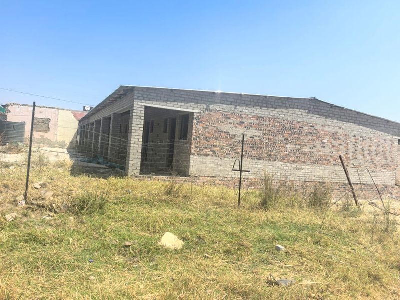 An unfinished exterior view of a residential building structure featuring exposed brick and concrete block walls with a corrugated metal roof.
