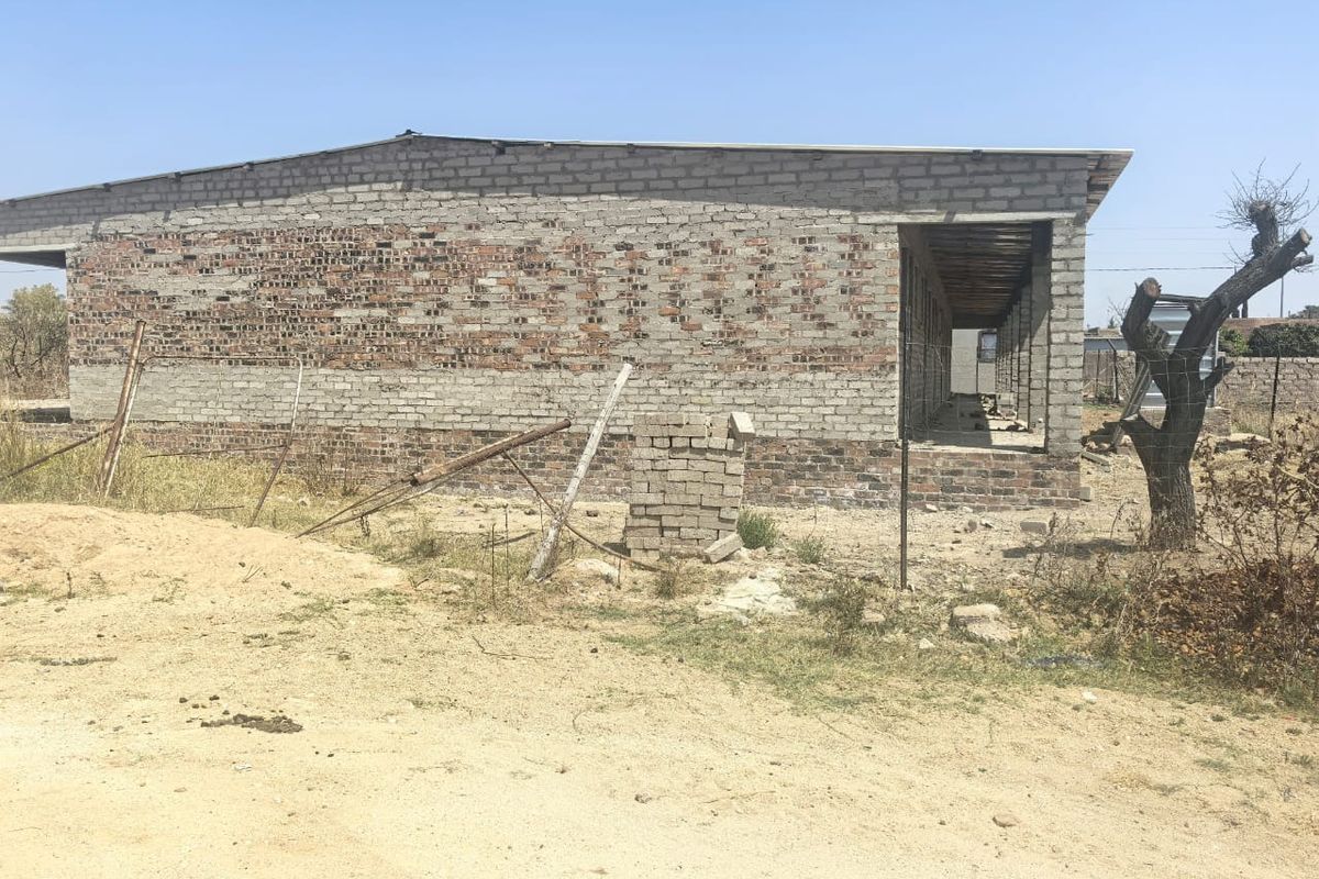An unfinished residential structure showing exposed brickwork and a metal roof, currently in the early stages of construction.